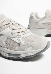 Beżowe sportowe buty sneakersy z połączeniem siateczki i zamszu, z wzmocnionym czubkiem, wyściełaną podeszwą i neutralnymi akcentami wzorniczymi.