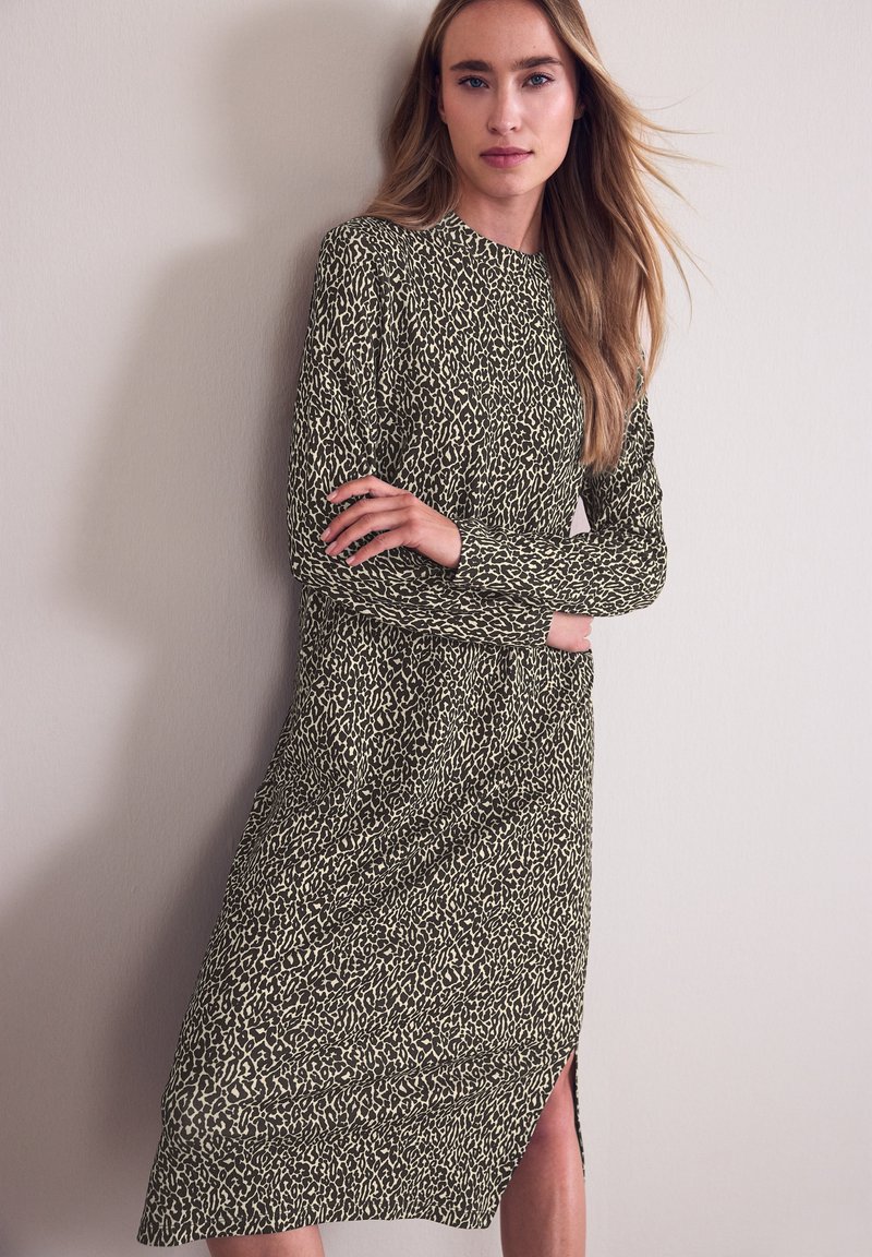 Robe ajustée à manches longues de couleur vert olive avec imprimé léopard noir ; elle présente un col rond et une fente latérale à l'ourlet.