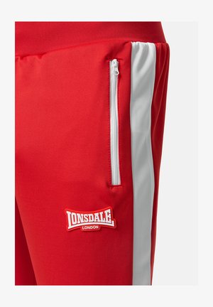 Pantaloni atletici rossi con tasca con zip, striscia laterale bianca e una spiccata patch del logo Lonsdale bianco e rosso. Textura del tessuto liscia.