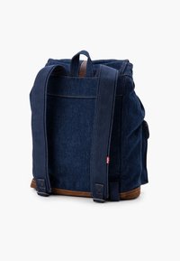 Tmavě modrý džínový batoh s hnědými koženými akcenty, dvěma širokými ramenními popruhy a pevným horním madlem. Jednoduchý design s viditelnými švy.