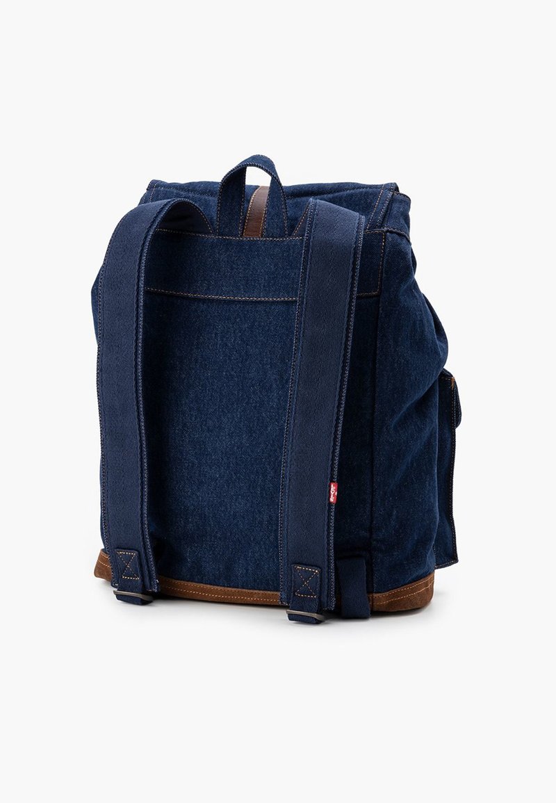 Zaino in denim blu scuro con dettagli in pelle marrone, due spallacci larghi e una robusta maniglia superiore. Design semplice con dettagli di cucitura visibili.