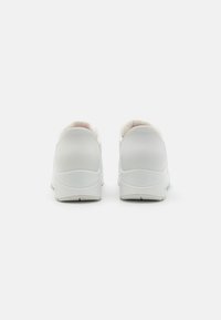 White sneakers with smooth synthetic material, rounded toe, padded collar, and textured rubber outsole. Minimalist design, no patterns.