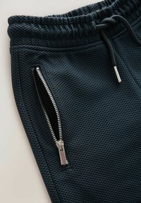 Joggeurs noirs en tissu texturé avec une poche zippée sur le côté, une taille élastique avec cordon de serrage et un tissu en maille respirant.