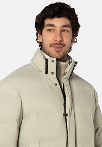 Hellbeige Steppjacke mit hohem Kragen, Druckknöpfen und einem Frontreißverschluss. Verfügt über eine glatte, isolierte Textur und eine moderne Passform.