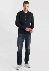 Cardigan noir boutonné avec col, présentant un design en tricot texturé. Associé à un jean bleu foncé et des baskets de couleur claire.