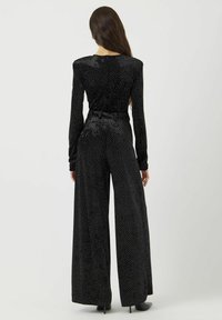 Mono de terciopelo negro con mangas largas, diseño de pierna ancha y patrón de lunares blancos, con cintura ajustada y un brillo sutil.