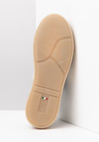 Beige rubber shoe sole with textured grip pattern, featuring an embossed logo and Italian flag detail. Design includes smooth and ridged sections.