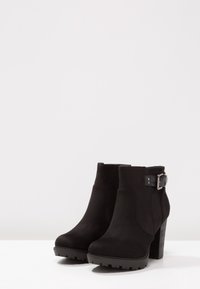 Bottines noires en daim, avec un talon épais et une boucle sur le côté. Texture lisse avec des semelles crantées pour une bonne adhérence.