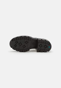 Suela de zapato de goma negra con surcos profundos, con seis patrones en cruz y un acento azul. Superficie lisa con una punta redondeada.