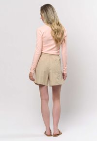 Világos rózsaszín bordázott hosszú ujjú felső és bézs rövidnadrág rugalmas derékrésszel, zsebekkel és laza szabással. A szettet szandál egészíti ki.