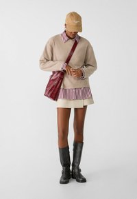 Beige trui over een gestreept shirt met bordeauxrood en wit, gecombineerd met een crèmekleurige rok en zwarte kniehooglaarzen. Bordeauxrode tas.