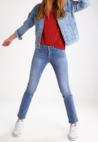 Ljusblå denimjeans med slim fit, medelhög midja och lätt slitage. Matchas med en röd t-shirt och denimjacka, bära med vita sneakers.