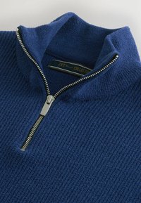Pulover din fleece albastru marin cu guler cu jumătate de fermoar, având o suprafață texturată cu riburi și un fermoar argintiu cu un tab acumulator metalic.