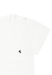 T-shirt bianco a maniche corte realizzato in tessuto morbido; presenta una tasca sul petto e due bottoni sulle spalle. Piccolo logo di una barca a vela blu sulla tasca.