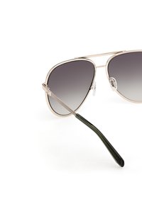Aviator-tyyliset aurinkolasit, joissa on harmaan sävyiset linssit, metallinen runko rose-kultaisena ja vihreät muoviset temput. Varustettu kaksoissillalla ja nenäpidikkeillä.