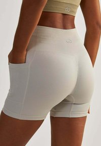 Shorts de sport gris clair avec une taille haute, texture côtelée et poches latérales. Présente un petit logo au-dessus de la poche droite.