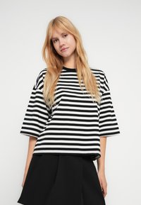 Μπλούζα με κοντά μανίκια σε ασπρόμαυρη ριγέ, με χαλαρή εφαρμογή και στρογγυλή λαιμόκοψη. Ομαλό ύφασμα με ομοιόμορφο μοτίβο σε όλη την επιφάνεια.