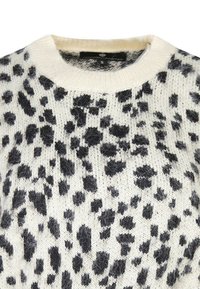 Maglione lavorato a maglia in crema con un design a macchie nere. Collo rotondo, texture morbida e vestibilità rilassata con dettagli di cucitura a vista.