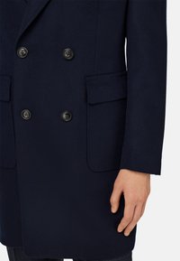 Abrigo doble faz de mezcla de lana en color navy, con seis botones de plástico negro, dos bolsillos frontales y una textura suave.