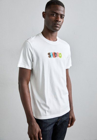 T-shirt en coton blanc arborant le mot "SANDRO" en lettres floues multicolores. Col rond classique et manches courtes.