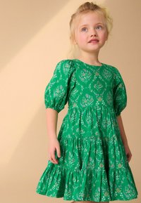 Abito floreale verde con maniche a sbuffo e gonna a strati. Realizzato in tessuto leggero con motivi floreali multicolori in tutta la superficie.