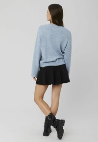 Pull en tricot bleu clair à épaules tombantes, associé à une jupe noire évasée. Bottes de combat noires épaisses avec un détail de boucle.