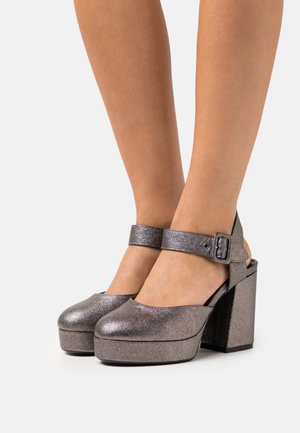 Chaussures plateforme en métal gris avec une sangle et une boucle, bout rond et un talon épais. Surface texturée avec une finition brillante.