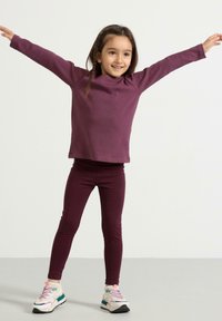 Lilla langærmet top med rund hals, parret med matchende leggings. Tøjet har en ribbet struktur. Sporty sneakers med multicolor detaljer.