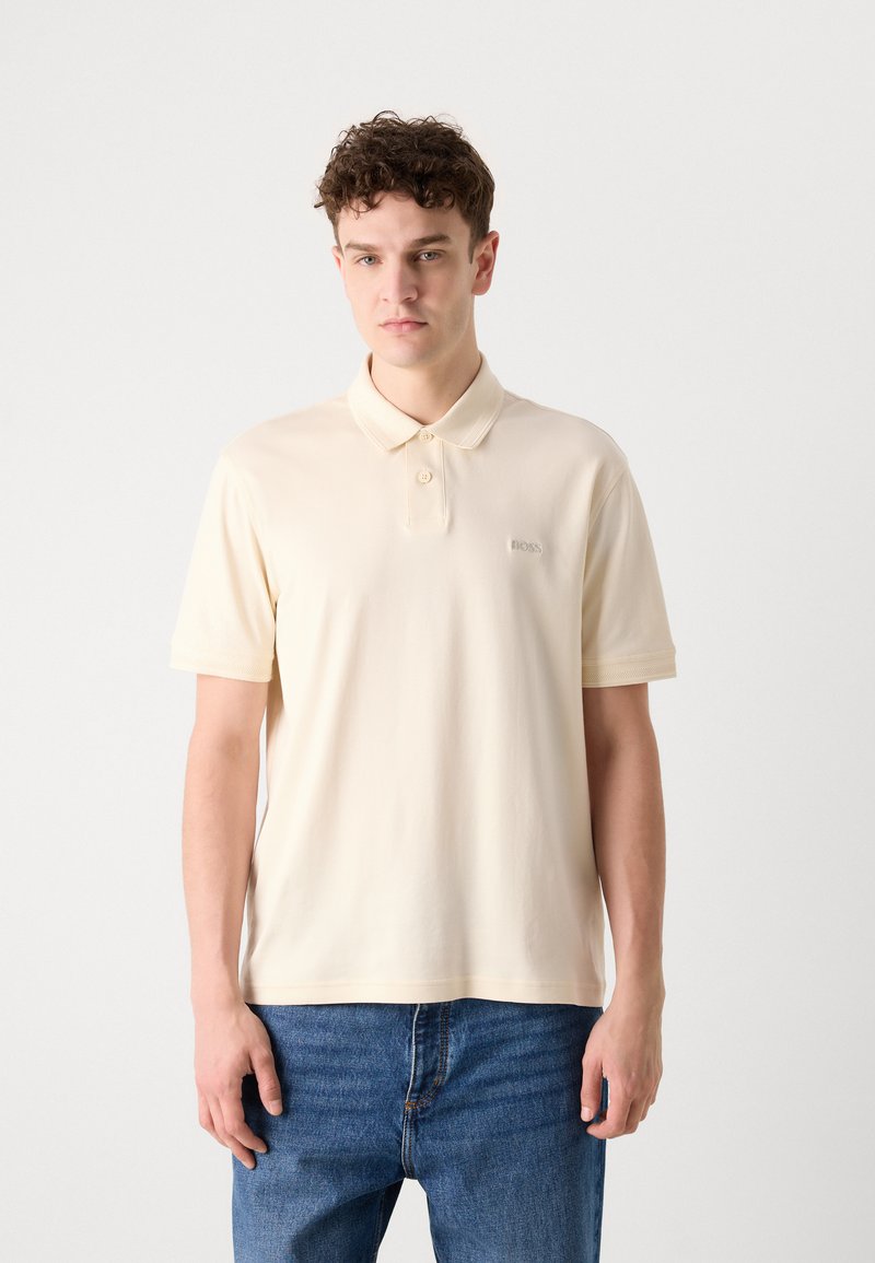 Polo-shirt à manches courtes en crème pâle, fabriqué en coton mélangé doux, avec une patte de boutonnage à deux boutons et un logo brodé sur la poitrine.