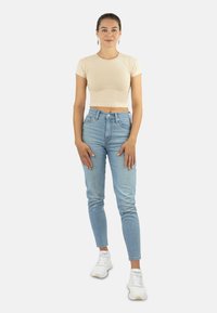 Beige verkürztes T-Shirt mit kurzen Ärmeln, kombiniert mit hellblauen hoch taillierten Jeans und weißen Sportschuhen.