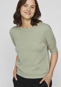 Pull court vert clair à manches courtes en tissu doux et texturé, avec un col rond et de légers détails bouffants sur les manches.