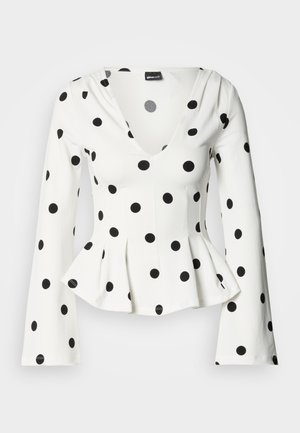 Hvit bluse med lange ermer og svarte polkadotter, med v-hals og peplum i midjen. Stoffet virker mykt med en jevn tekstur.