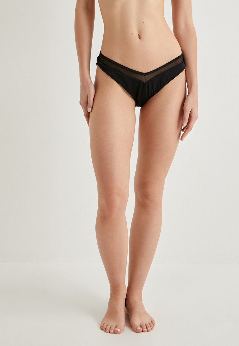 Parte inferior de bikini negra con un diseño en forma de V, paneles de malla translúcida y tejido suave y elástico para mayor comodidad y ajuste.