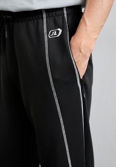 Pantalons de sport noirs ajustés, dotés de rayures blanches sur les côtés, d'un logo brodé et d'une poche zippée pour le rangement.