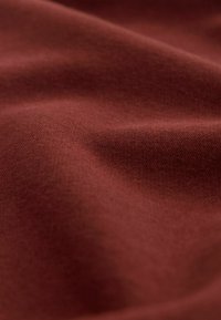 Bruin gestructureerde stof met een zacht, licht gerimpeld oppervlak, die een warme, rijke kleur en gladheid toont, typisch voor katoen of een katoenmengsel.