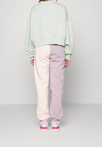 Mátově zelené oversize mikiny spárované s kalhotami na jógu v pastelových barvách – růžové a fialové. Bílé tenisky s růžovými akcenty dotvářejí celkový vzhled.