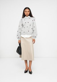 Hallide hall sweatsärk punaste südame mustritega, all valge kraepealne särk, beež nahkne seelik, must kott ja terava ninaga mustad kontsad.