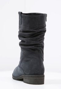 Bota de cuero negro de altura media con caña suelta, detalles de costura y un tacón bajo de madera sobre fondo blanco.