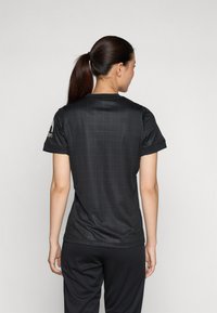 Maillot noir à manches courtes avec un motif en grille, texture lisse, col rond et logo sur l'épaule gauche, associé à un pantalon noir.