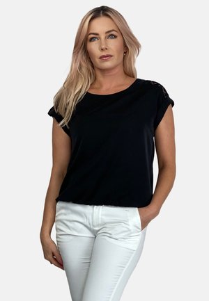 Czarny top z krótkim rękawem z koronkowymi detalami na ramionach, w zestawieniu z białymi dopasowanymi spodniami. Gładki materiał, luźny krój, okrągły dekolt.