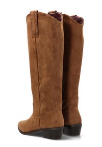 Botas de ante marrón hasta la rodilla con un acabado texturizado, punta redondeada y tacón bajo en bloque. Tachuelas decorativas recorren la parte trasera para un detalle adicional.