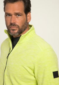 Pullover in pile giallo fluorescente con design a mezze zip, tessuto testurizzato e patch nera a contrasto sulla manica.