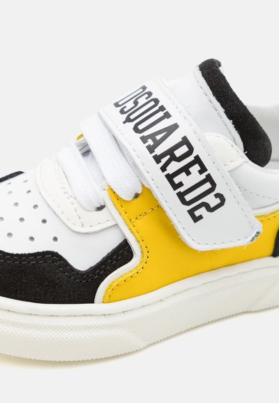 Sneaker in pelle bianca, camoscio nero e dettagli gialli. Presenta una pattina in velcro e una punta forata per la traspirabilità.
