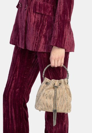 Bolso de ante beige con detalles en tono plateado, que presenta un cierre de cordón y patrones decorativos de brillantes, sostenido con un asa metálica.