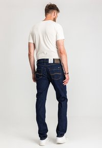 Granatowe dżinsy o prostym kroju, tylne kieszenie z detalami w postaci przeszyć, noszone z jasnokolorową koszulką i białymi trampkami.