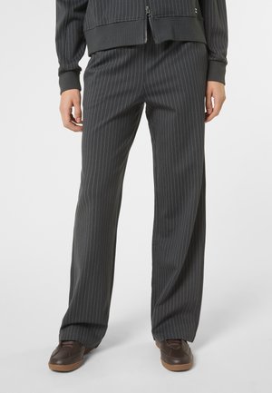 Onderlichaam gekleed in donkergrijze, gestreepte, wijd uitlopende broek met bruine schoenen, gecombineerd met een bijpassend jas met ritssluiting.