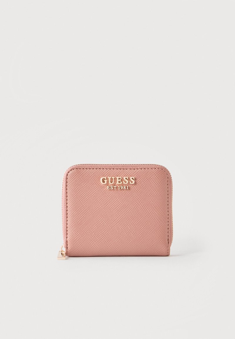 Portefeuille rose texturé avec fermeture éclair sur tout le pourtour et logo doré "GUESS EST 1981" sur le devant, sur un fond clair uni.