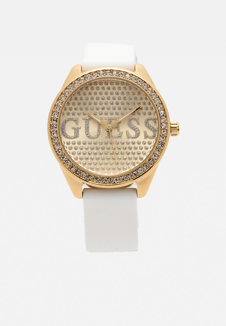 Reloj color dorado con correa de silicona blanca. Cuenta con una esfera plateada punteada y detalles de cristal alrededor del bisel y el logotipo. Forma redonda clásica.