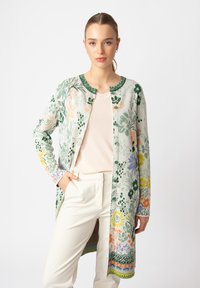 Kvetinový cardigan s zeleným základom a multicolornými kvetinovými vzormi, okrúhlym výstrihom a dlhými rukávmi. Materiál vyzerá mäkký a ľahký.