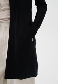 Zwarte cardigan van zachte stof, met lange mouwen, geribbelde boorden en zijzakken. Het kledingstuk heeft een rechte zoom en een ontspannen pasvorm.